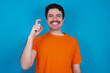 © Roquillo - young handsome Caucasian man with moustache wearing orange t-shirt against blue background pointing up with fingers number nine in Chinese sign language Jiu