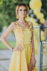 Poster - Vertical portrait of a gorgeous Caucasian blonde female in elegant yellow dress posing in the street