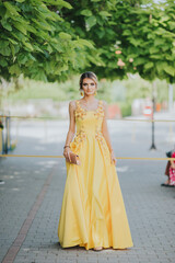 Poster - Vertical portrait of a gorgeous Caucasian blonde female holding her elegant yellow dress in street