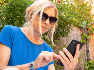 Wall Mural - Closeup shot of a blonde woman in sunglasses looking at the phone