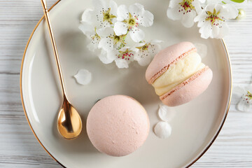 Delicious pink macarons and flowers on white wooden table, flat lay