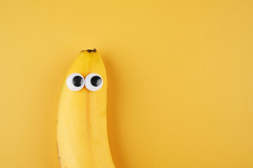 Funny banana with eyes concept isolated on yellow background with copy space