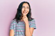Hispanic teenager girl with dental braces wearing casual clothes with hand on chin thinking about question, pensive expression. smiling with thoughtful face. doubt concept.