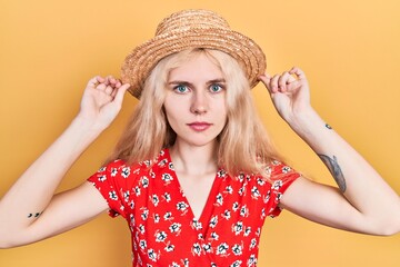 Wall Mural - Beautiful caucasian woman with blond hair wearing summer hat relaxed with serious expression on face. simple and natural looking at the camera.