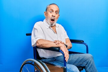 Poster - Handsome senior man with beard sitting on wheelchair in shock face, looking skeptical and sarcastic, surprised with open mouth