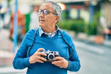 Wall Mural - senior grey-haired tourist man smiling happy using vintage camera at the city.