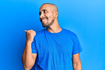 Canvas Print - Hispanic adult man wearing casual blue t shirt pointing thumb up to the side smiling happy with open mouth