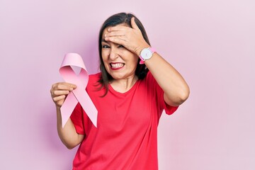 Poster - Middle age hispanic woman holding pink cancer ribbon stressed and frustrated with hand on head, surprised and angry face