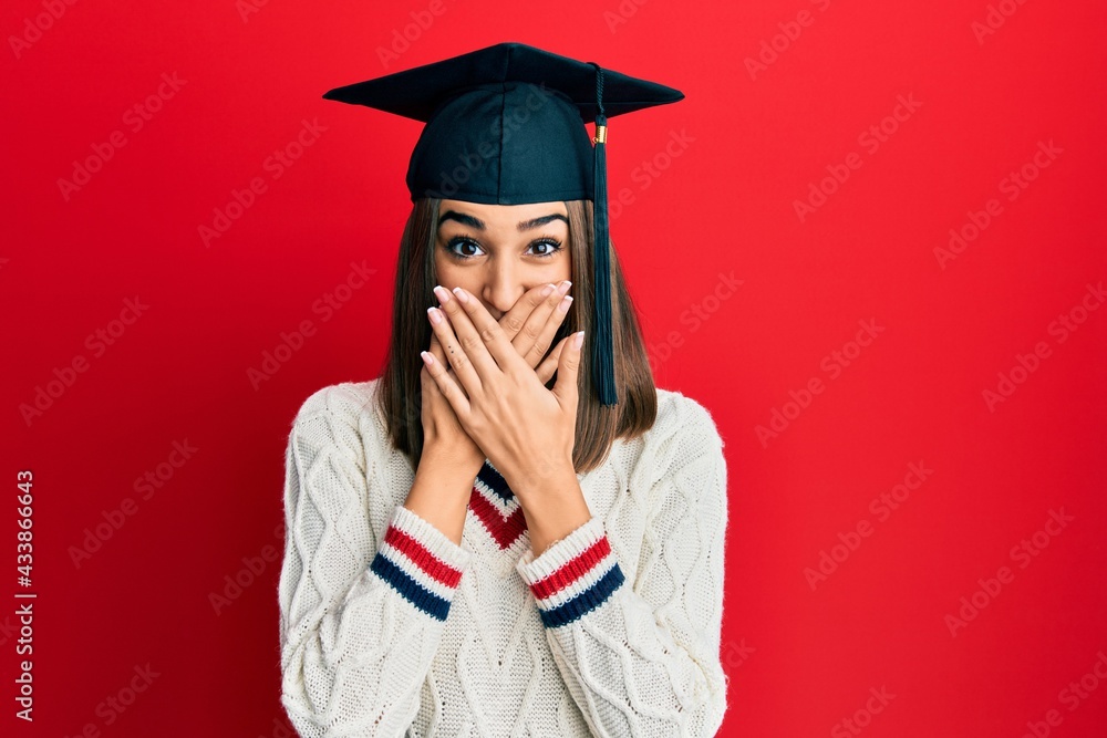 Young brunette girl wearing graduation cap shocked covering mouth with ...