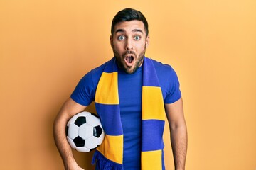 Canvas Print - Young hispanic man football hooligan soccer ball scared and amazed with open mouth for surprise, disbelief face