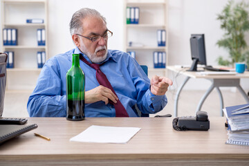 Old male employee drinking alcohol in the office