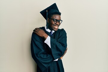 Wall Mural - Handsome black man wearing graduation cap and ceremony robe hugging oneself happy and positive, smiling confident. self love and self care