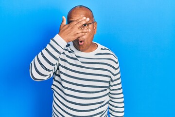 Middle age latin man wearing casual clothes and glasses peeking in shock covering face and eyes with hand, looking through fingers with embarrassed expression.