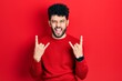 © Krakenimages.com - Young arab man with beard wearing casual red sweater shouting with crazy expression doing rock symbol with hands up. music star. heavy concept.