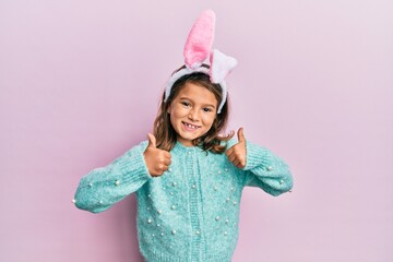 Little beautiful girl wearing cute easter bunny ears success sign doing positive gesture with hand, thumbs up smiling and happy. cheerful expression and winner gesture.