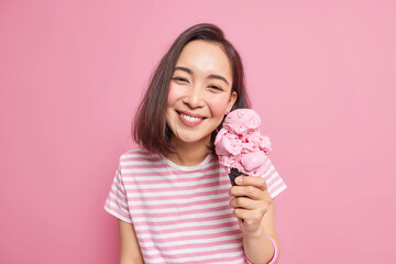 Wall Mural - lovely dark haired asian woman enjoys eating tasty strawberry ice cream during hot summer day has up