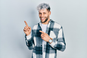 Young hispanic man with modern dyed hair wearing casual shirt smiling and looking at the camera pointing with two hands and fingers to the side.