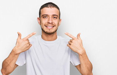 Hispanic young man wearing casual white t shirt smiling cheerful showing and pointing with fingers teeth and mouth. dental health concept.