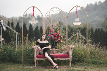 Wall Mural - Woman wearing black dress sitting on the couch on flowers garden.