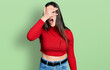 © Krakenimages.com - Young brunette teenager wearing red turtleneck sweater peeking in shock covering face and eyes with hand, looking through fingers with embarrassed expression.