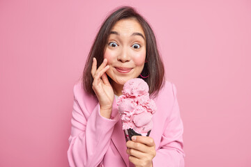 Wall Mural - Summer is here. Pretty lovely brunette young eastern woman holds big strawberry ice cream in waffle enjoys eating delicious frozen dessert wears fashionable jacket isolated over pink background