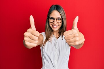 Wall Mural - Young brunette woman wearing casual clothes and glasses approving doing positive gesture with hand, thumbs up smiling and happy for success. winner gesture.