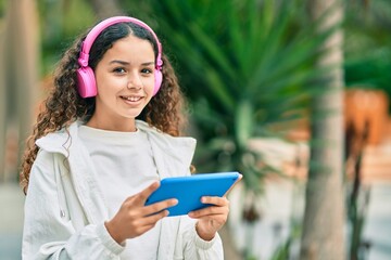 Wall Mural - Hispanic child girl smiling happy using headphones and touchpad at the city.