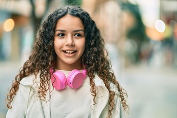 Wall Mural - Hispanic child girl smiling happy using headphones at the city.