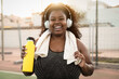 © Alessandro Biascioli - Happy curvy African woman doing jogging and workout routine while listening music with wireless headphones outdoor
