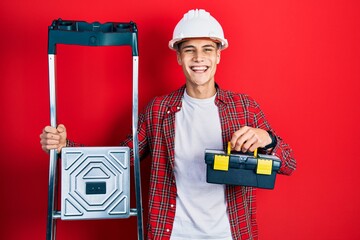 Sticker - Young hispanic man holding tools box wearing hardhat by construction stairs celebrating crazy and amazed for success with open eyes screaming excited.