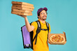 Portrait of a young courier, pizza delivery man in uniform with a thermo backpack holding pizza boxes isolated on a blue background. Fast home delivery. Online order.