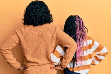 Wall Mural - Beautiful african american mother and daughter wearing wool winter sweater standing backwards looking away with arms on body