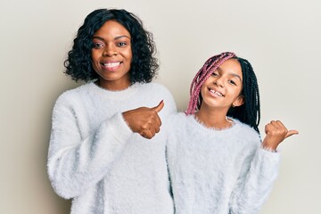 Canvas Print - Beautiful african american mother and daughter wearing casual winter sweater pointing to the back behind with hand and thumbs up, smiling confident