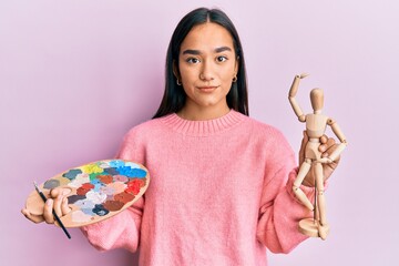 Poster - Young asian woman holding painter palette and art manikin relaxed with serious expression on face. simple and natural looking at the camera.