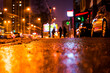 Rainy night in the big city, the street with walking people and parked cars. Close up view from the asphalt level
