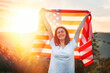 Independence day. A happy caucasian young woman holds an American flag in her hands, raised above her head. Sunset in the background. The concept of American National Holidays