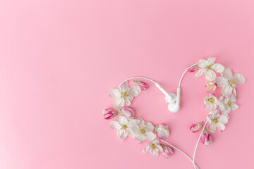 Flat lay on pink background with apple blossom heart shape and earphones