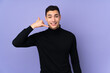 © luismolinero - Young caucasian handsome man with turtleneck sweater isolated on purple background making phone gesture. Call me back sign