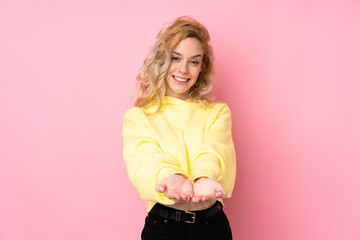 Poster - Young blonde woman wearing a sweatshirt isolated on pink background holding copyspace imaginary on the palm to insert an ad