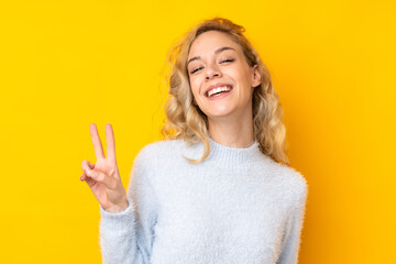 Poster - Young blonde woman isolated on yellow background smiling and showing victory sign