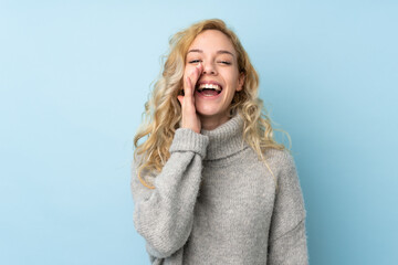 Wall Mural - Young blonde woman wearing a sweater isolated on blue background shouting with mouth wide open