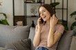 © kucherav - Beautiful young cute caucasian woman enjoys pleasant mobile conversation on the mobile phone while sitting at home on the couch