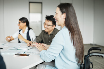 Wall Mural - Side view portrait of smiling businesswoman in wheelchair enjoying meeting with colleagues in office