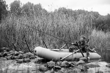 Wall Mural - View of a fisherman rod fish on the river on a rubber boat. Black and white photo.