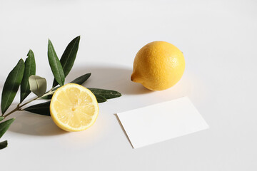 Wall Mural - Summer stationery still life scene. Cut lemon fruit and olive tree branch nad leaves in sunlight. Blank business card mockup isolated on white table background. Branding concept, Mediterranean design