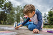 © Miljan Živković - Small caucasian boy four years old sitting on the concrete pavement drawing with chalk in park in day childhood and growing up education concept