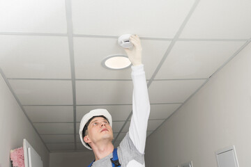 Wall Mural - a worker installs a fire safety sensor on a suspended ceiling