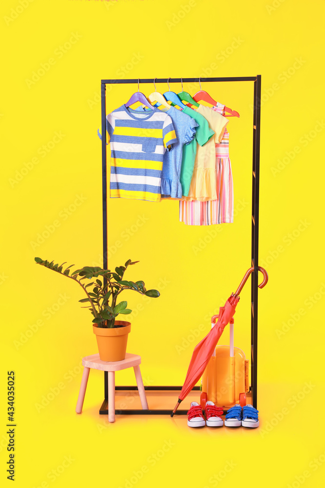 Rack with clothes and houseplant on color background