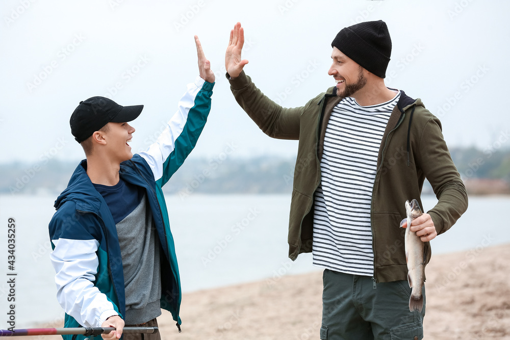 Happy father and son with caught fish on river bank