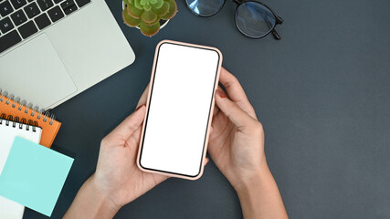 Poster - Hands of businesswoman holding smart phone with blank screen on her workspace.